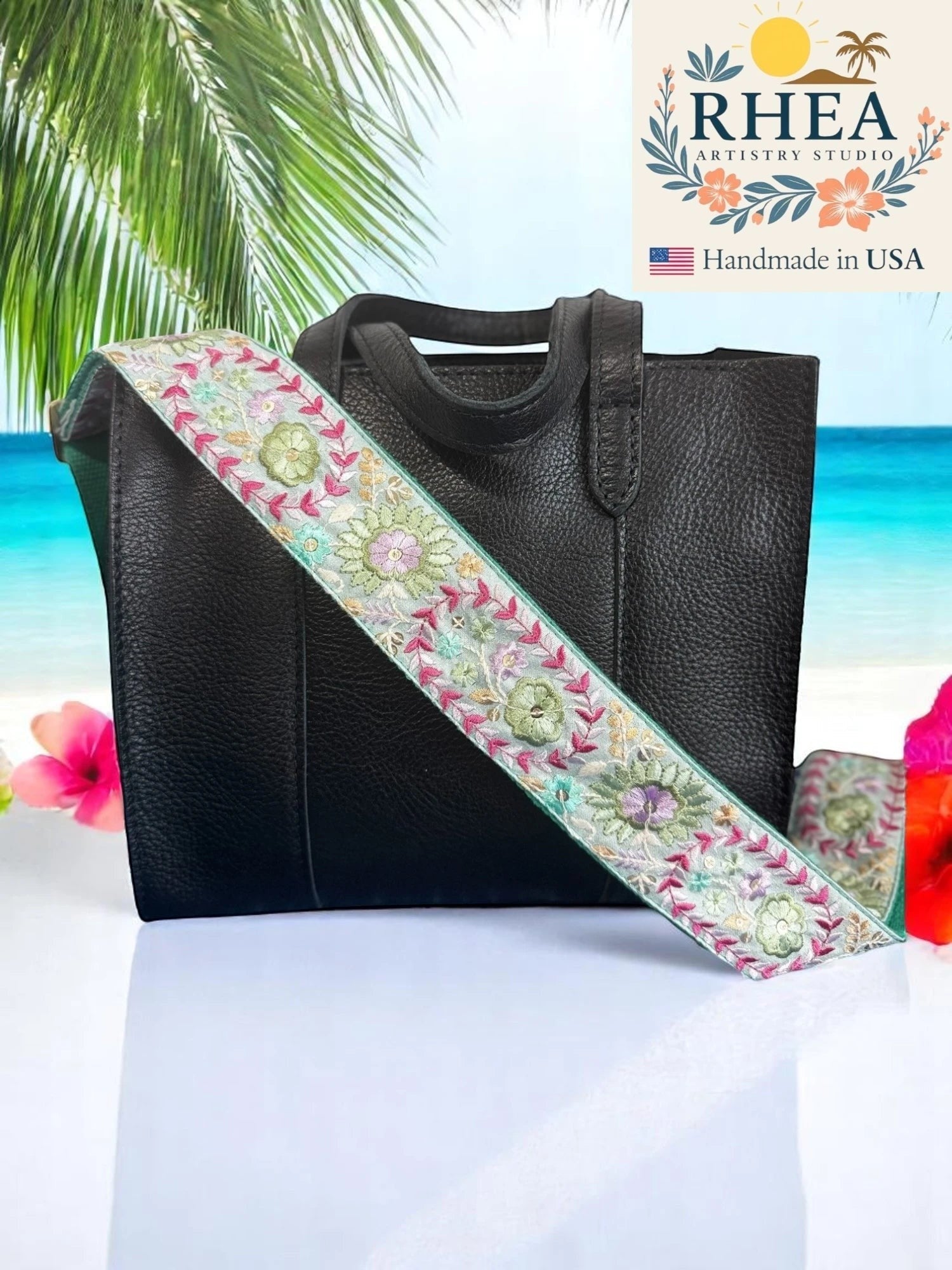 Rhea Artistry Studio 2-inch wide crossbody strap with Dahlia embroidery in pastel pink, green, and purple on a light grey background. Adjustable strap with brushed brass hardware.