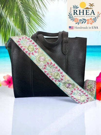 Rhea Artistry Studio 2-inch wide crossbody strap with Dahlia embroidery in pastel pink, green, and purple on a light grey background. Adjustable strap with brushed brass hardware.