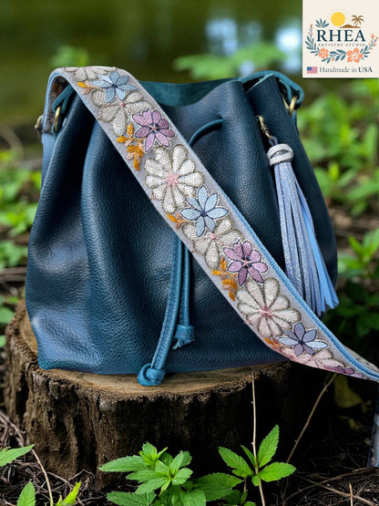 Rhea Artistry Studio 2-inch crossbody strap with embroidered daisies in pastel colors on a grey background, adjustable length.