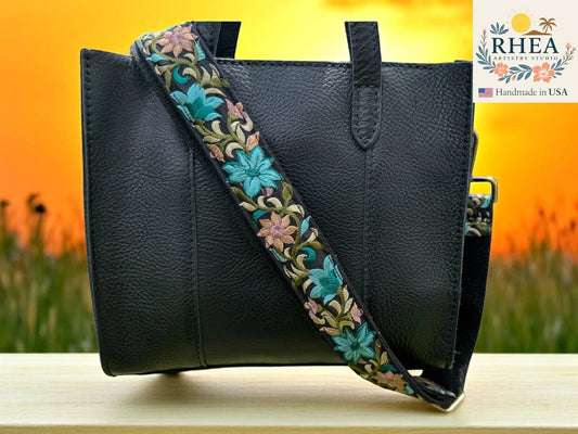 Rhea Artistry Studio black leather bag with a 1.5-inch wide adjustable crossbody strap featuring vibrant floral embroidery in teal, pink, and green.