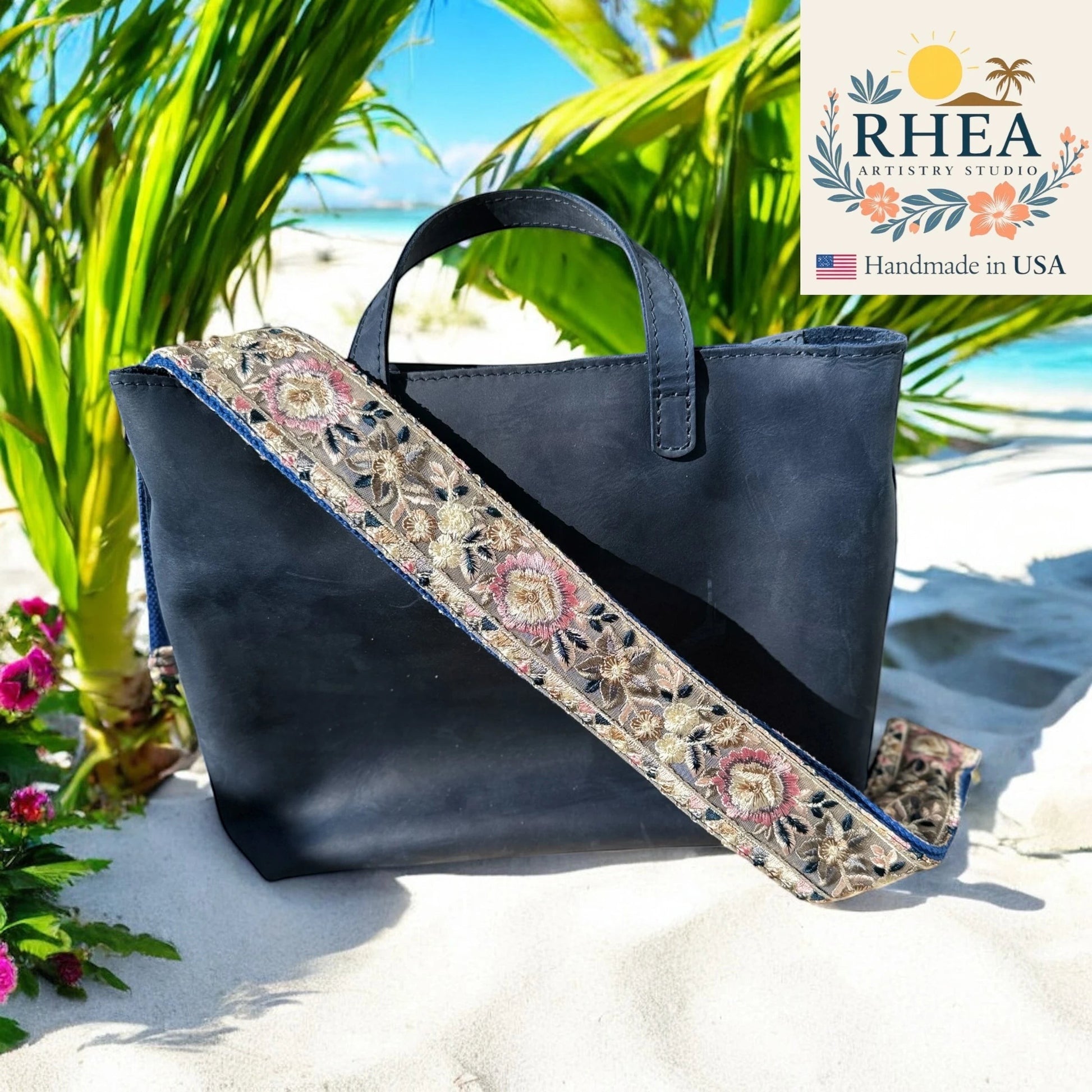 Rhea Artistry Studio navy blue leather tote bag with a 2-inch wide adjustable embroidered floral strap in pink, gold, and blue.