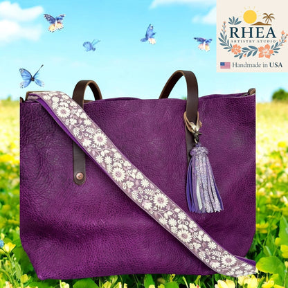 Rhea Artistry Studio purple leather tote bag with a 1.5-inch adjustable crossbody strap featuring white floral embroidery and a purple tassel.