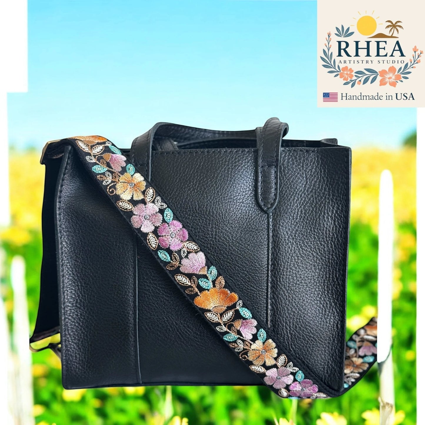 Rhea Artistry Studio black crossbody strap with embroidered floral pattern in pink, orange, and blue, 1.5-inch width, adjustable length.