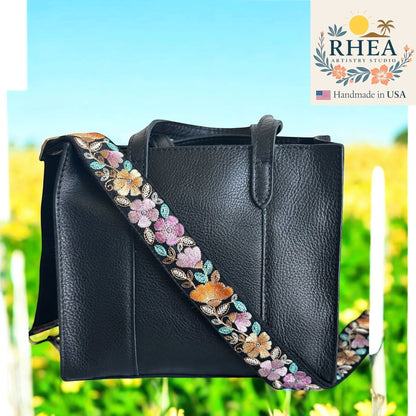 Rhea Artistry Studio black crossbody strap with embroidered floral pattern in pink, orange, and blue, 1.5-inch width, adjustable length.