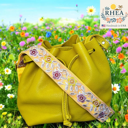 Rhea Artistry Studio 2-inch crossbody strap with embroidered colorful florals on a light yellow background, attached to a lime green leather bucket bag.