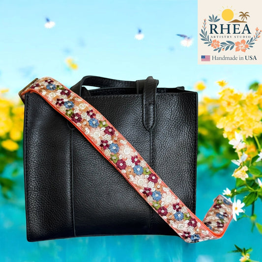 Rhea Artistry Studio embroidered crossbody strap with floral pattern in cream, blue, and burgundy on a coral edge.