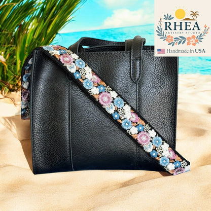 Rhea Artistry Studio black crossbody bag with a 1.5-inch adjustable embroidered strap featuring blue, pink, and white floral patterns.