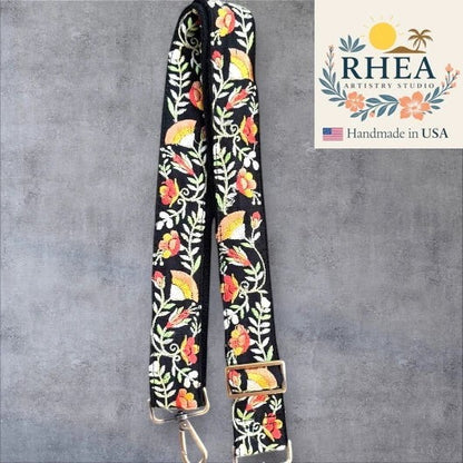 Rhea Artistry Studio black crossbody strap with embroidered floral and fan motifs in coral, yellow, and green. Adjustable length with brushed brass hardware.