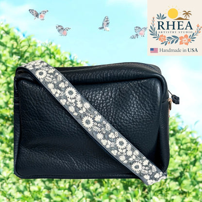 Rhea Artistry Studio navy crossbody bag with a 1.5-inch adjustable strap featuring white floral embroidery and brushed brass hardware.