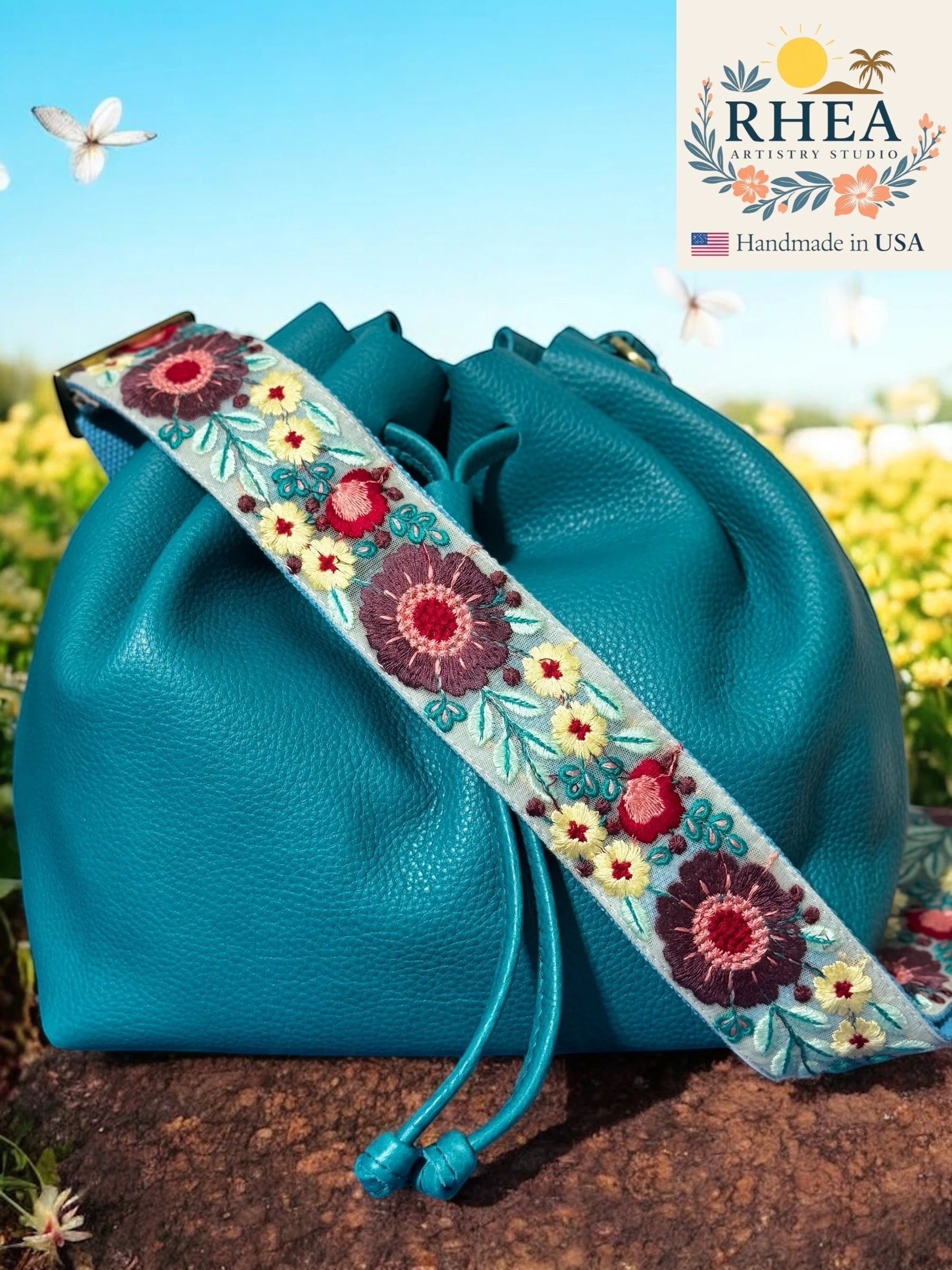 Rhea Artistry Studio 2-inch crossbody strap with embroidered floral lace in burgundy, yellow, and teal on a light blue background. Adjustable.