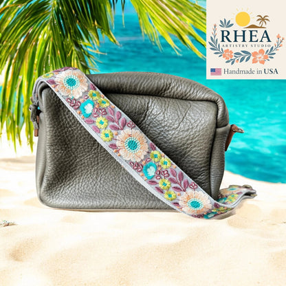 Rhea Artistry Studio grey leather crossbody bag with a 2-inch wide embroidered floral lace strap in pastel colors. Adjustable strap with brass hardware.