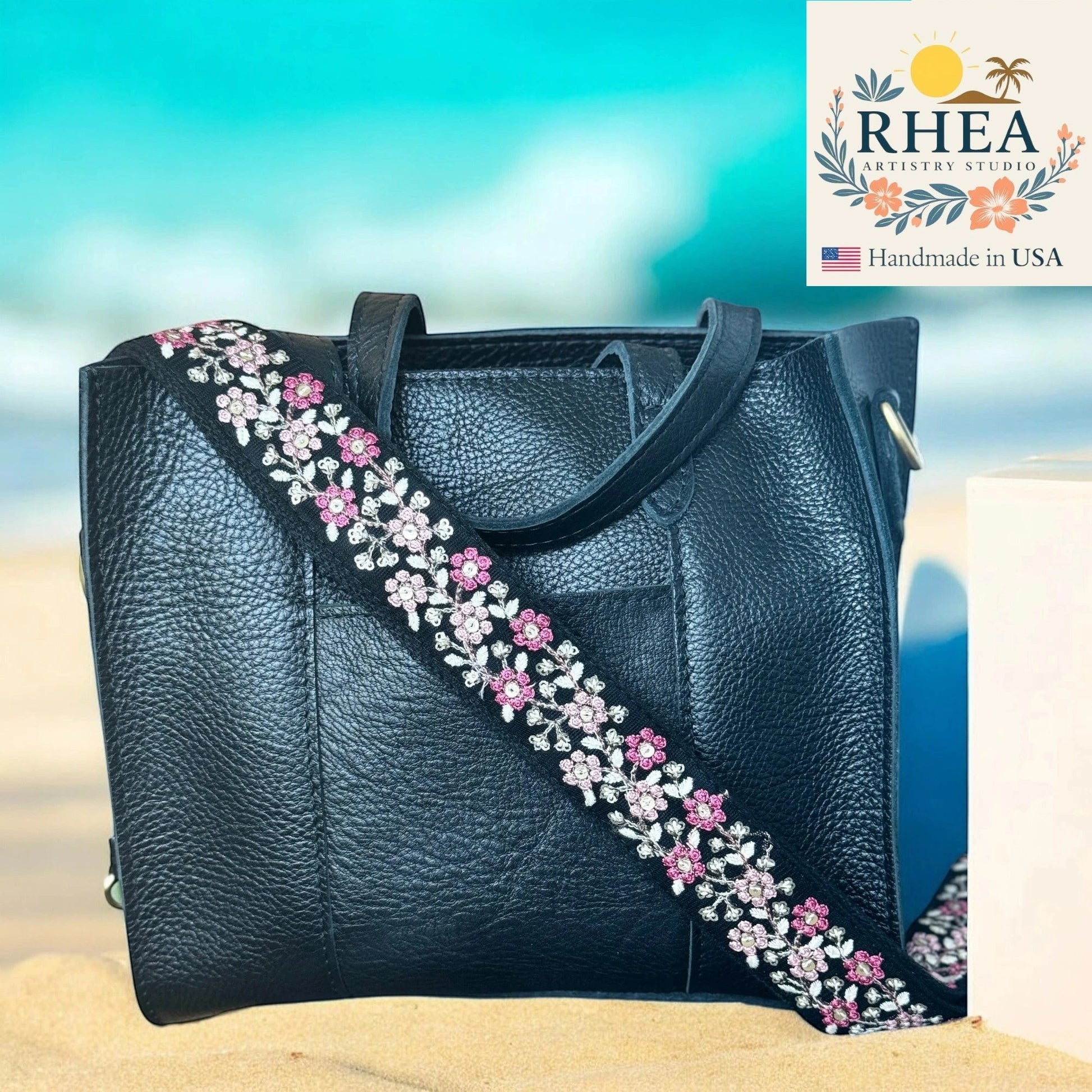 Rhea Artistry Studio black crossbody strap with pink and white floral embroidery, 1.5-inch width, adjustable length.