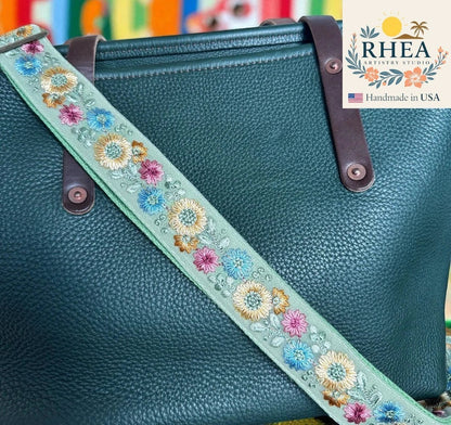 Rhea Artistry Studio light green crossbody strap with embroidered floral pattern in pink, blue, and yellow. Adjustable strap with brushed brass hardware.