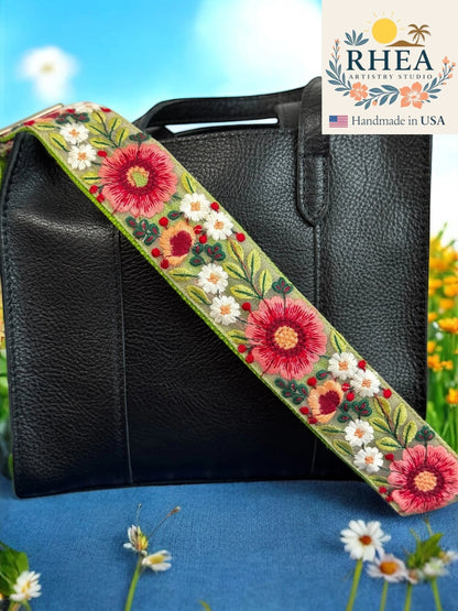 Rhea Artistry Studio 2-inch crossbody strap with embroidered floral lace in pink, white, and coral on a light green background. Adjustable strap with brass hardware.