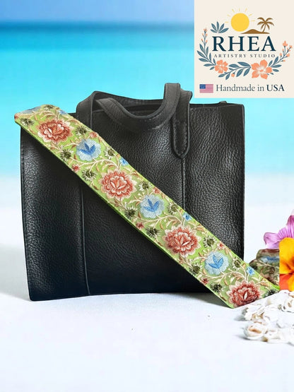 Rhea Artistry Studio 2-inch wide crossbody strap with green background and embroidered floral pattern in pink, blue, and coral. Adjustable length with brass hardware.