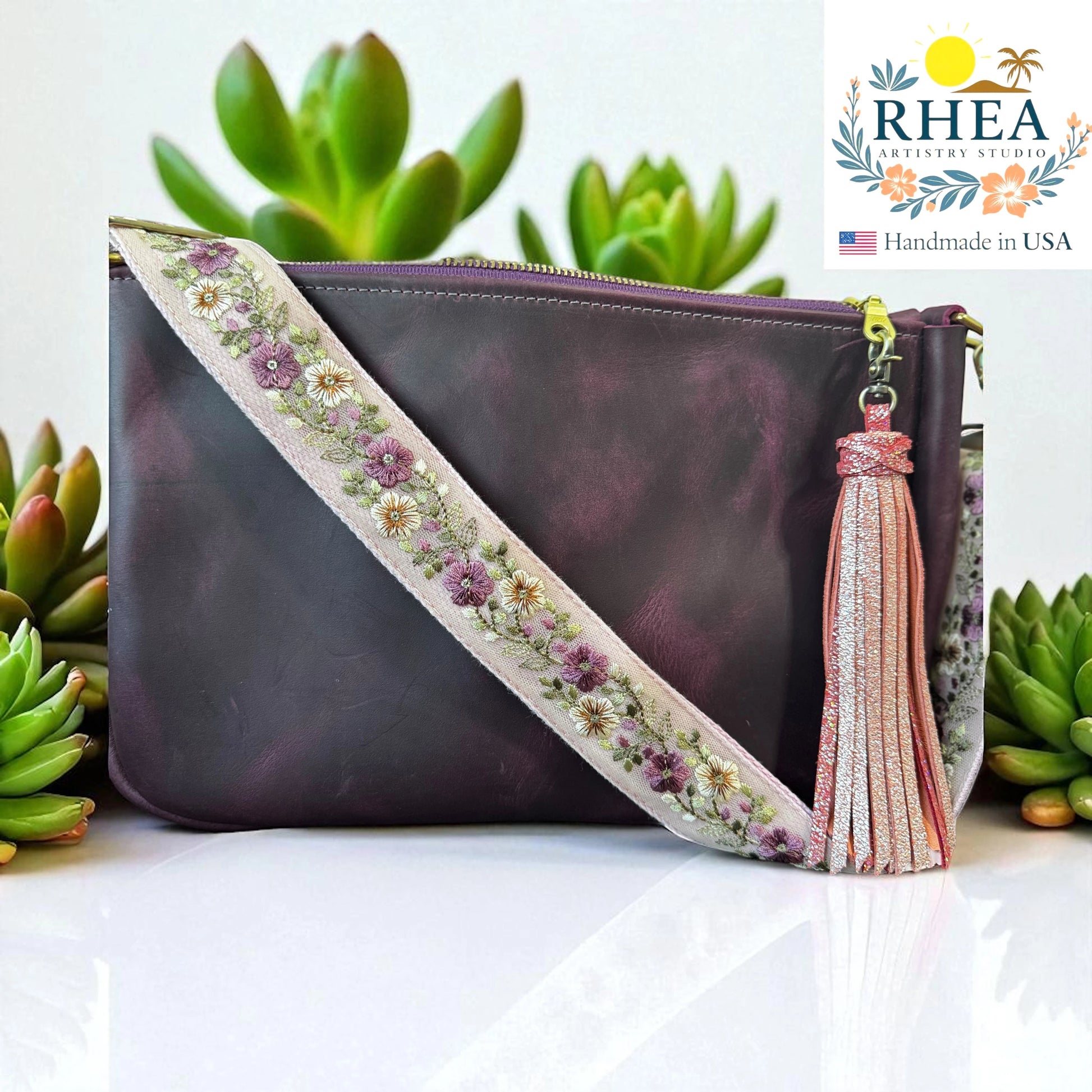 Rhea Artistry Studio 1.5-inch crossbody strap with blush and ivory floral embroidery on light beige fabric, brushed brass hardware, and adjustable length.