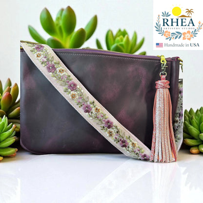 Rhea Artistry Studio 1.5-inch crossbody strap with blush and ivory floral embroidery on light beige fabric, brushed brass hardware, and adjustable length.