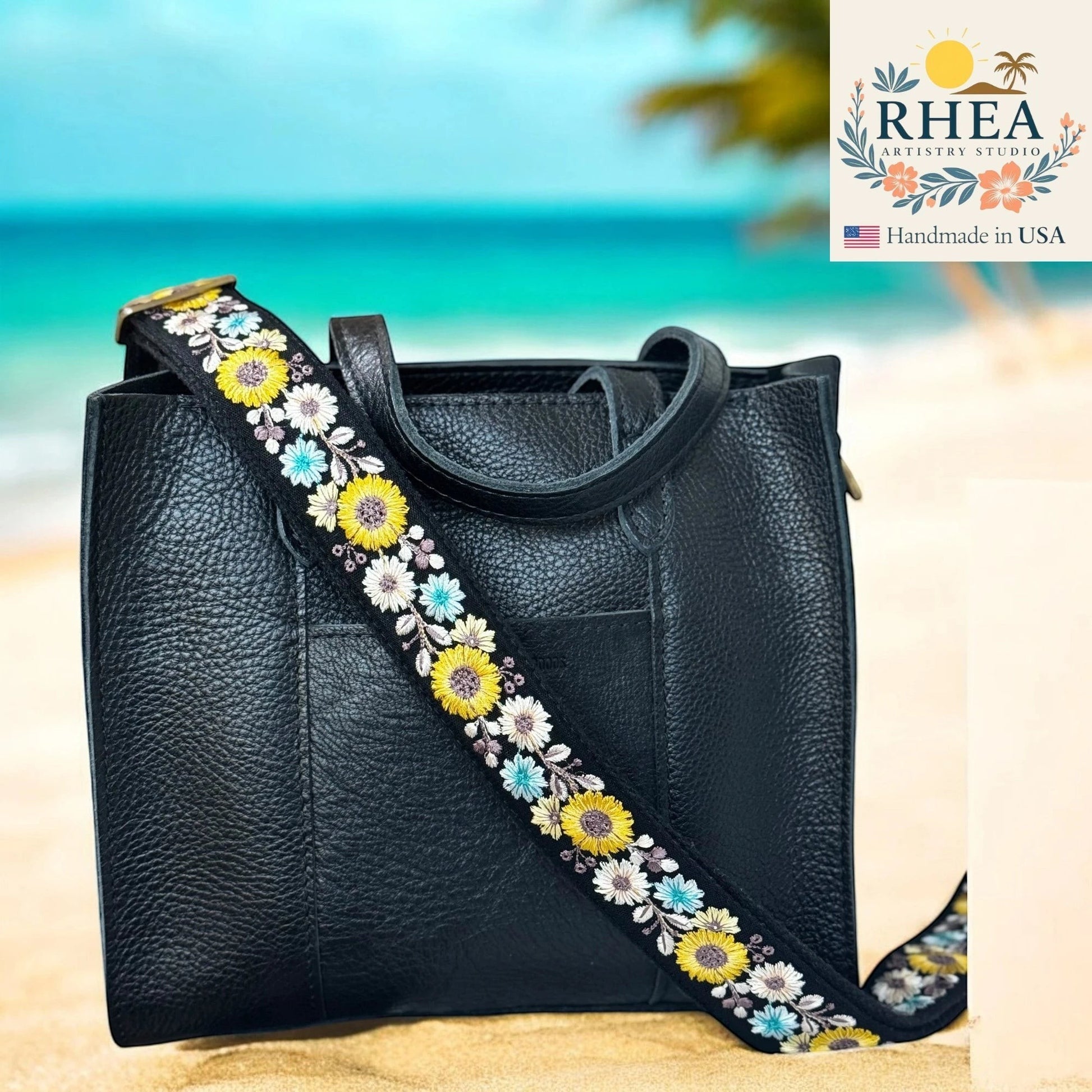 Rhea Artistry Studio black crossbody strap with embroidered yellow, white, and blue flowers, 1.5-inch wide with brushed brass hardware.