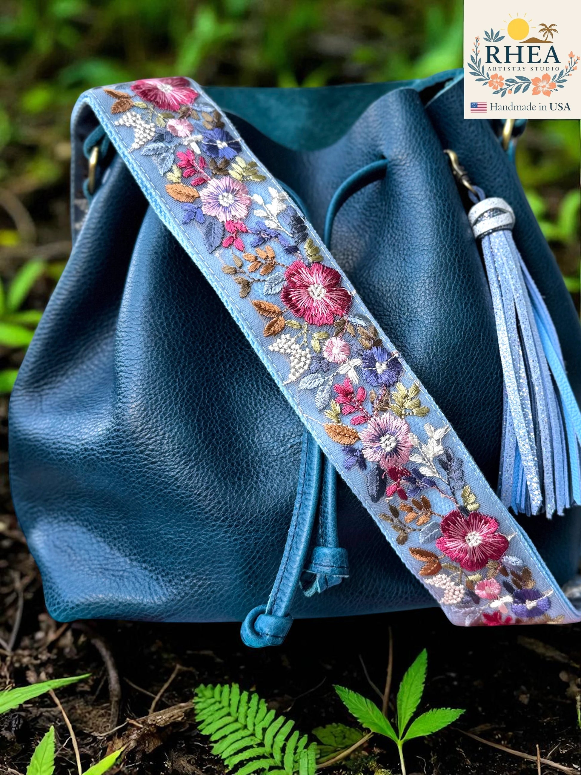 Rhea Artistry Studio light blue crossbody strap with vibrant floral embroidery, 2-inch width, adjustable length, and brushed brass hardware.