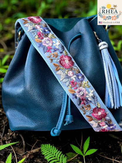 Rhea Artistry Studio light blue crossbody strap with vibrant floral embroidery, 2-inch width, adjustable length, and brushed brass hardware.