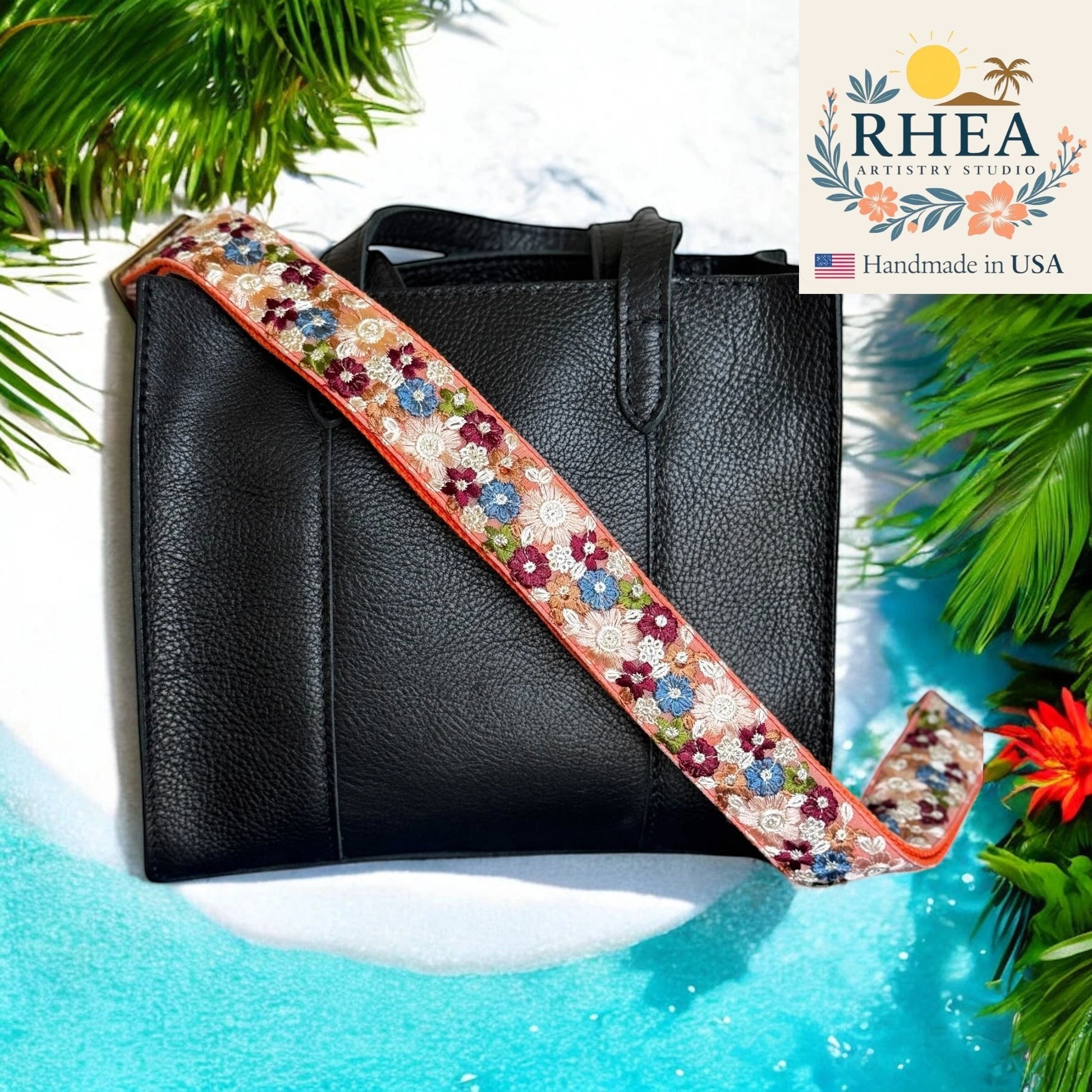 Rhea Artistry Studio crossbody strap with embroidered floral pattern in cream, pink, blue, and burgundy on a peach background.