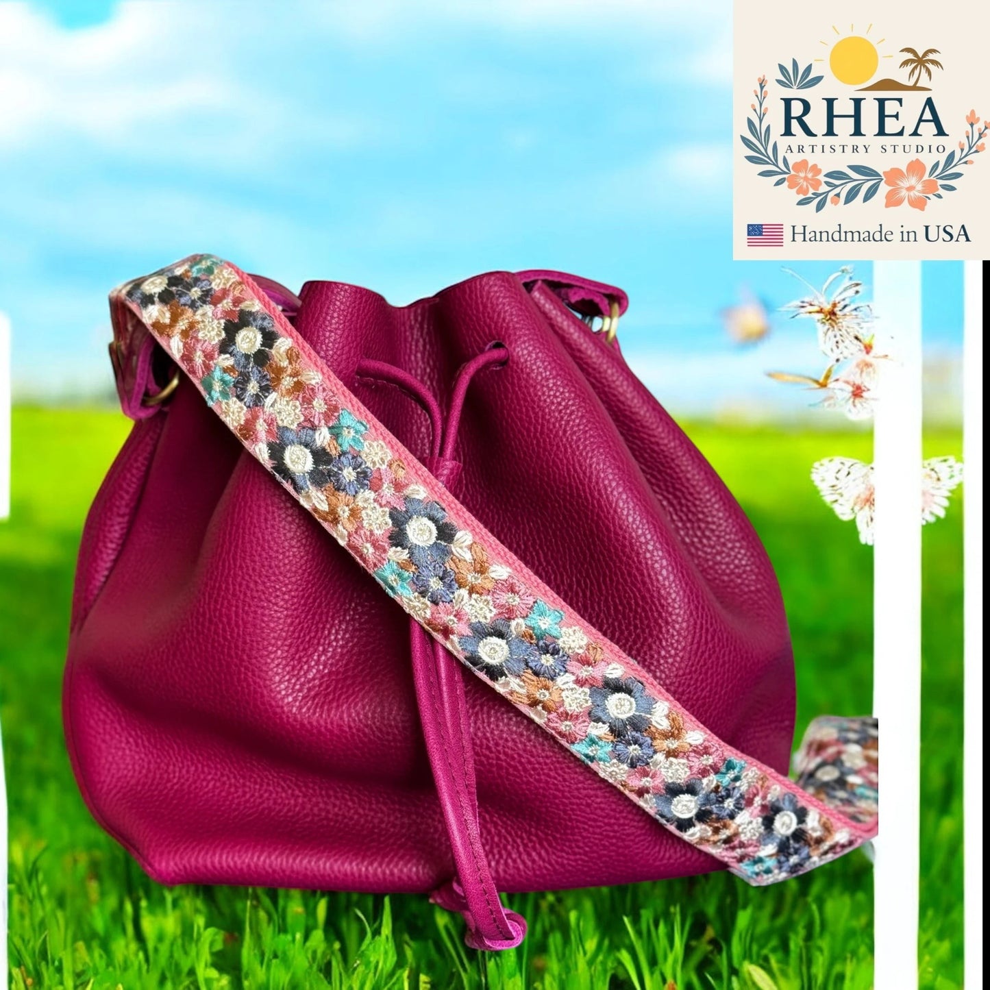 Rhea Artistry Studio crossbody strap with embroidered floral pattern on cream base and pink leather trim, attached to a magenta bucket bag.