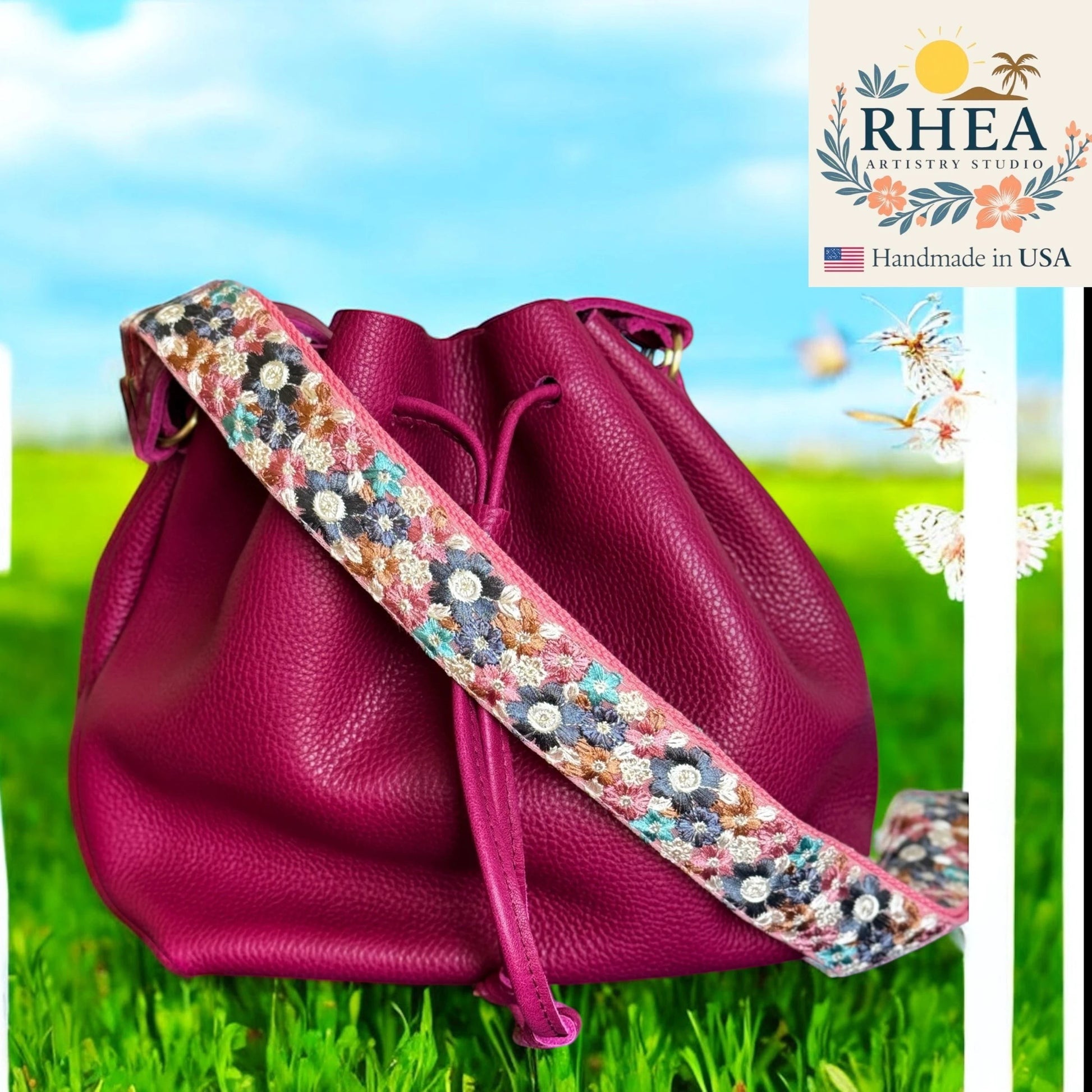 Rhea Artistry Studio crossbody strap with embroidered floral pattern on cream base and pink leather trim, attached to a magenta bucket bag.
