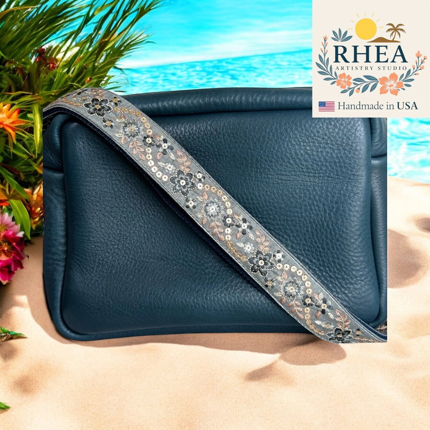 Rhea Artistry Studio navy blue leather crossbody bag with a 1.5-inch embroidered floral strap in grey with silver and pink accents.