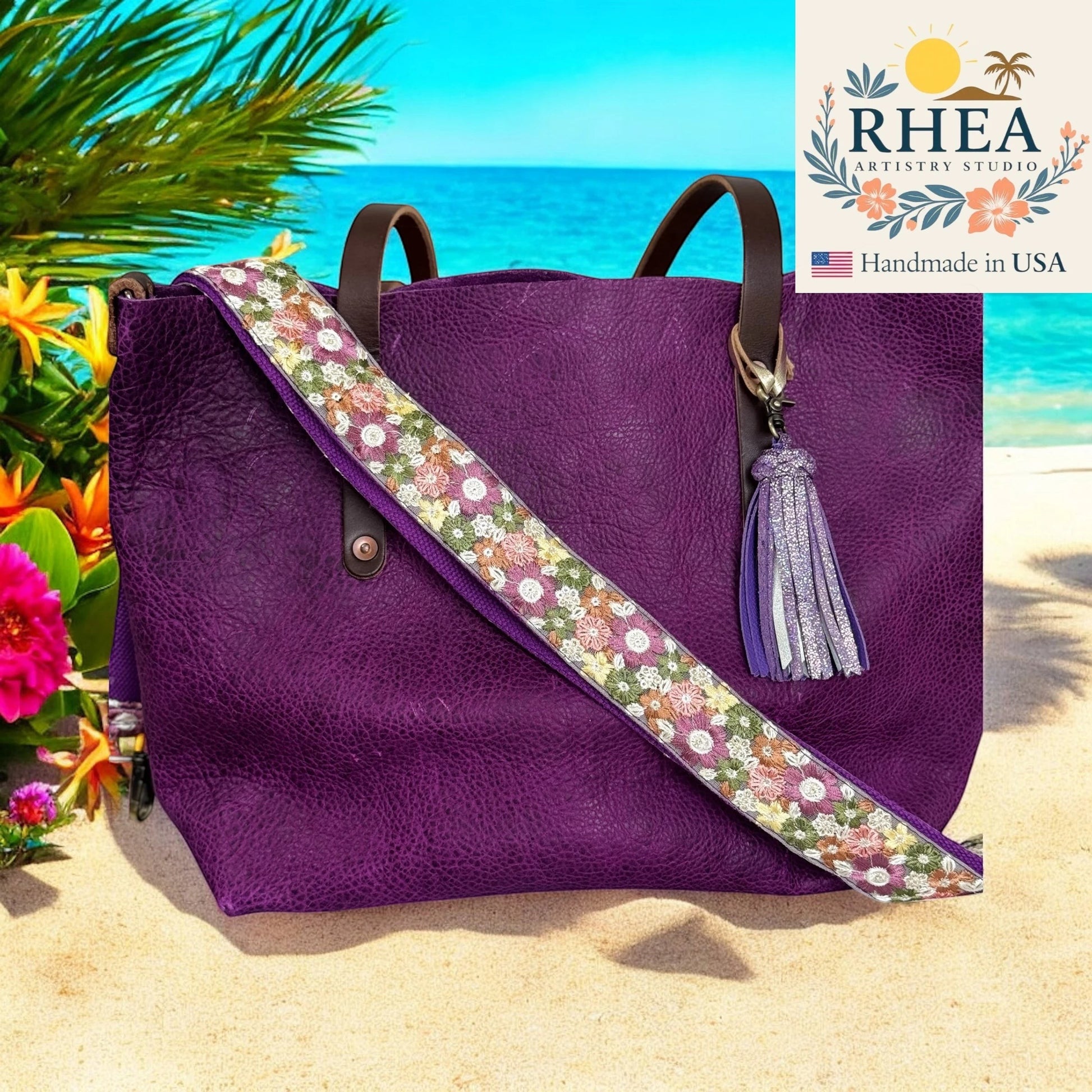 Rhea Artistry Studio purple leather tote with embroidered floral crossbody strap and tassel, set on a beach.