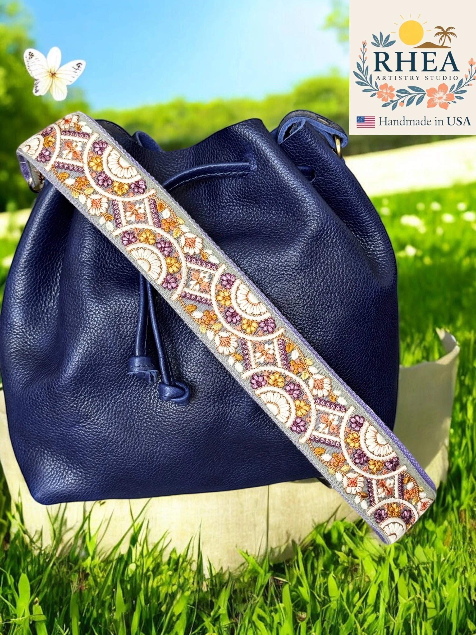 Rhea Artistry Studio 2-inch wide crossbody strap with embroidered floral lace in purple, orange, and yellow on a grey background.