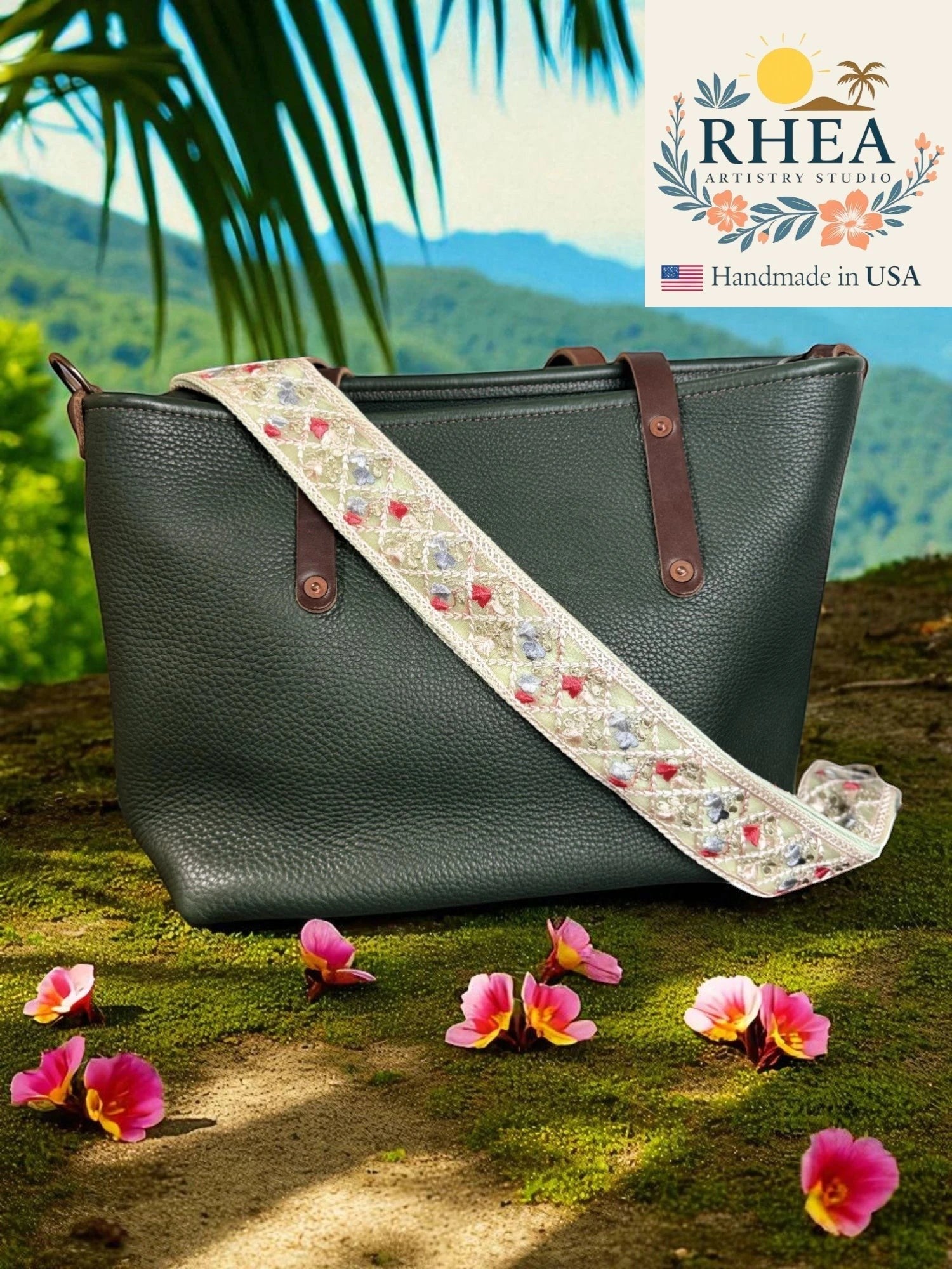 Rhea Artistry Studio 2-inch wide crossbody strap with embroidered floral lace in pastel colors and diamond pattern, attached to a dark green pebbled leather tote bag.