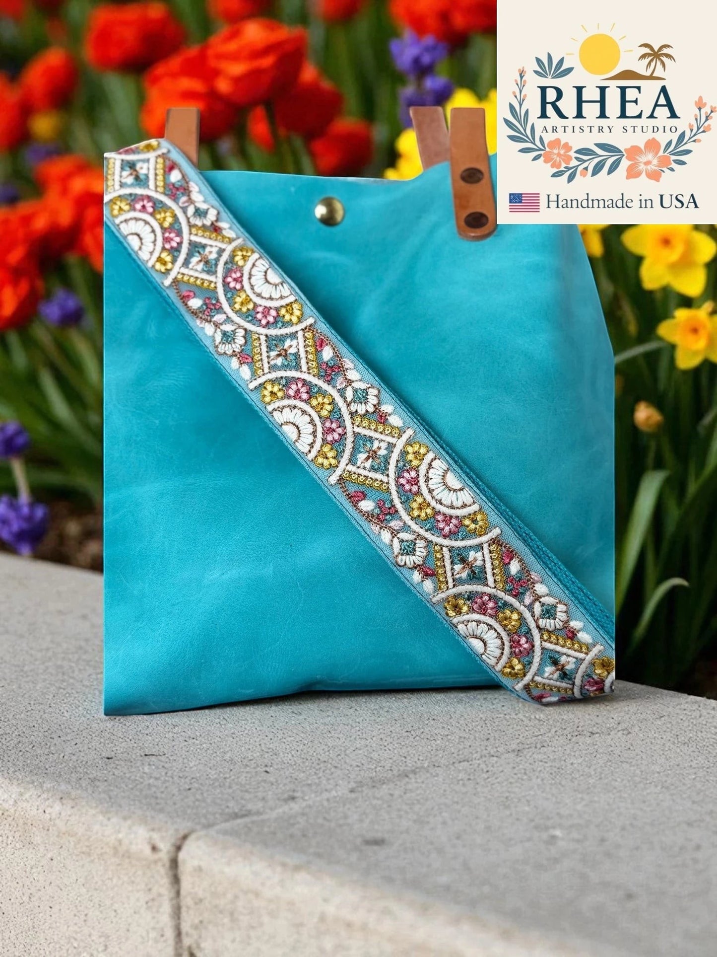Rhea Artistry Studio 2-inch crossbody strap with embroidered floral lace in blue, pink, and yellow on a light blue background.