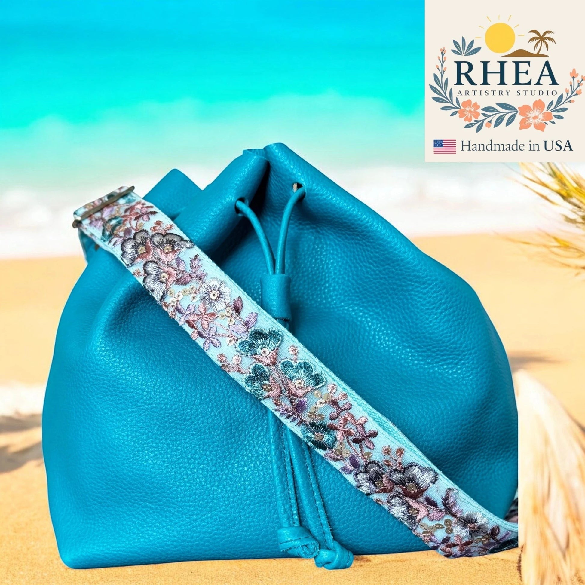 Rhea Artistry Studio turquoise leather bucket bag with a 1.5-inch adjustable crossbody strap featuring embroidered floral lace in blue, pink, and purple.