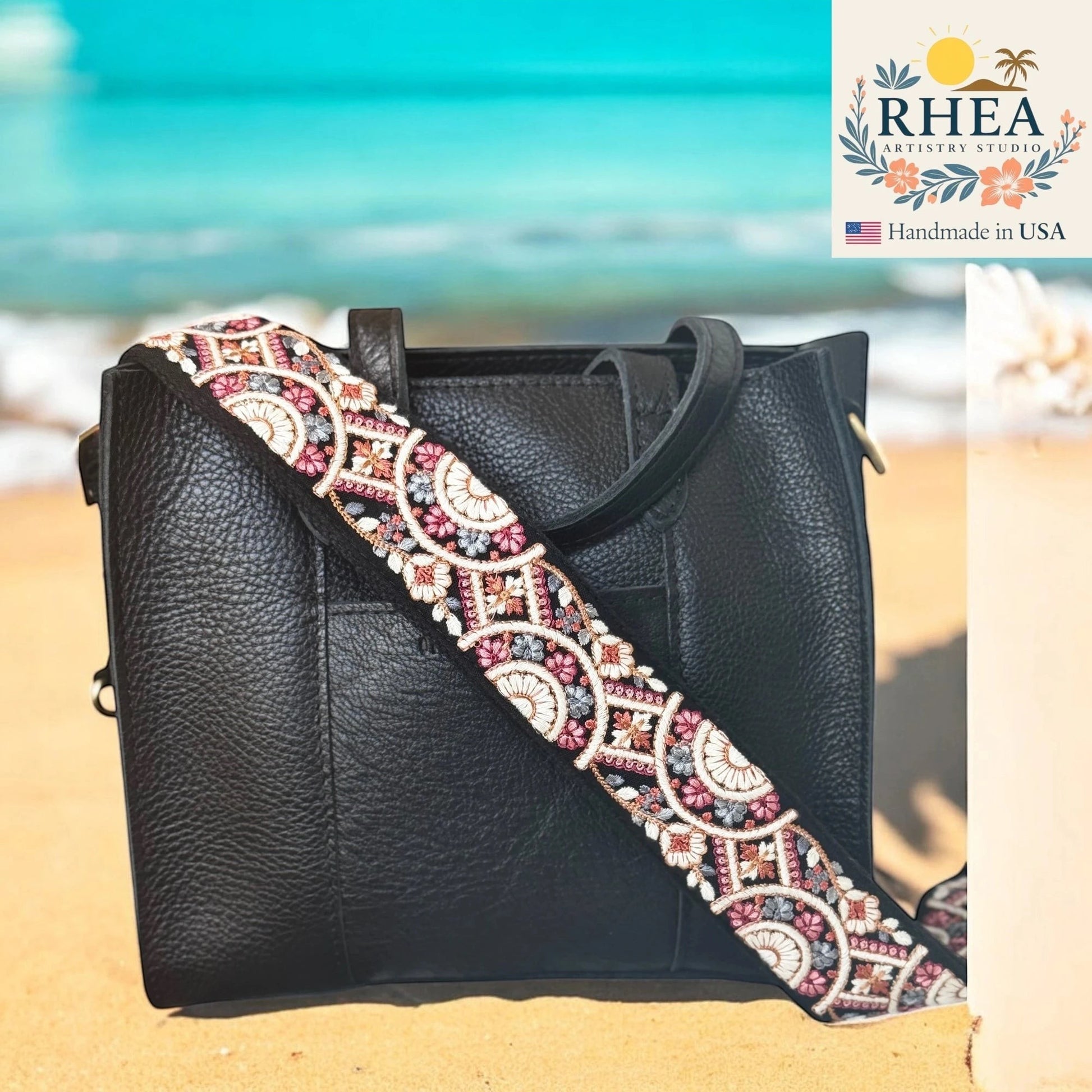 Rhea Artistry Studio 2-inch crossbody strap with embroidered floral lace in pink, white, and grey on black webbing. Adjustable length with brass hardware.
