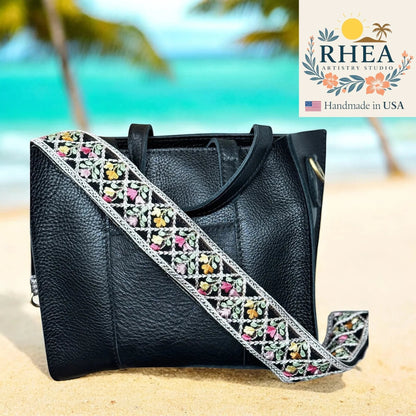 Rhea Artistry Studio black leather handbag with a 2-inch wide crossbody strap featuring embroidered floral lace in pink, yellow, and green.