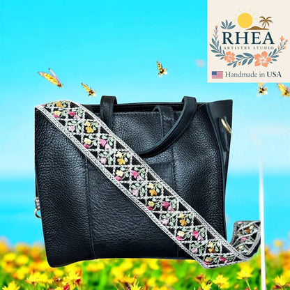 Rhea Artistry Studio black leather handbag with a 2-inch wide embroidered floral lace strap in pastel colors. Adjustable crossbody strap.