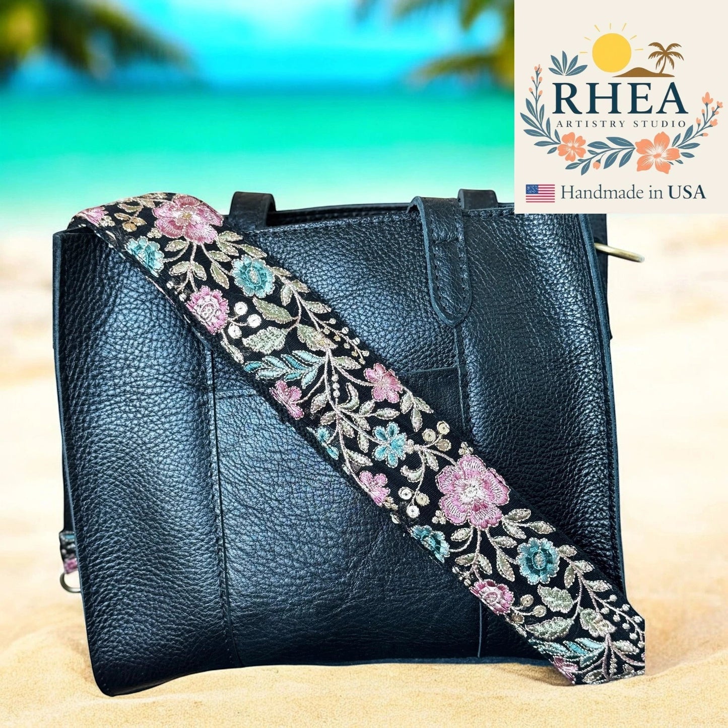 Rhea Artistry Studio 2-inch wide black crossbody strap with embroidered pink, blue, and gold floral fern pattern. Adjustable.