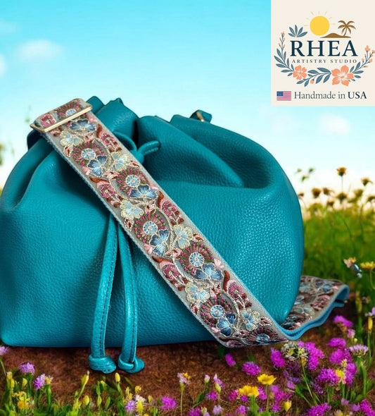 Rhea Artistry Studio turquoise crossbody bag with a 2-inch wide adjustable strap featuring intricate floral embroidery in pink, blue, and gold.