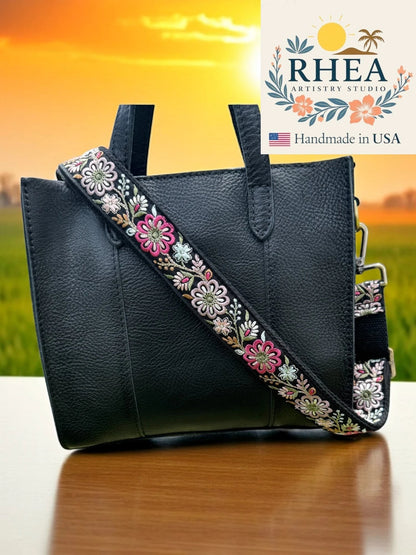 Rhea Artistry Studio black crossbody bag with a 1.5-inch adjustable strap featuring colorful embroidered pinwheel flowers.
