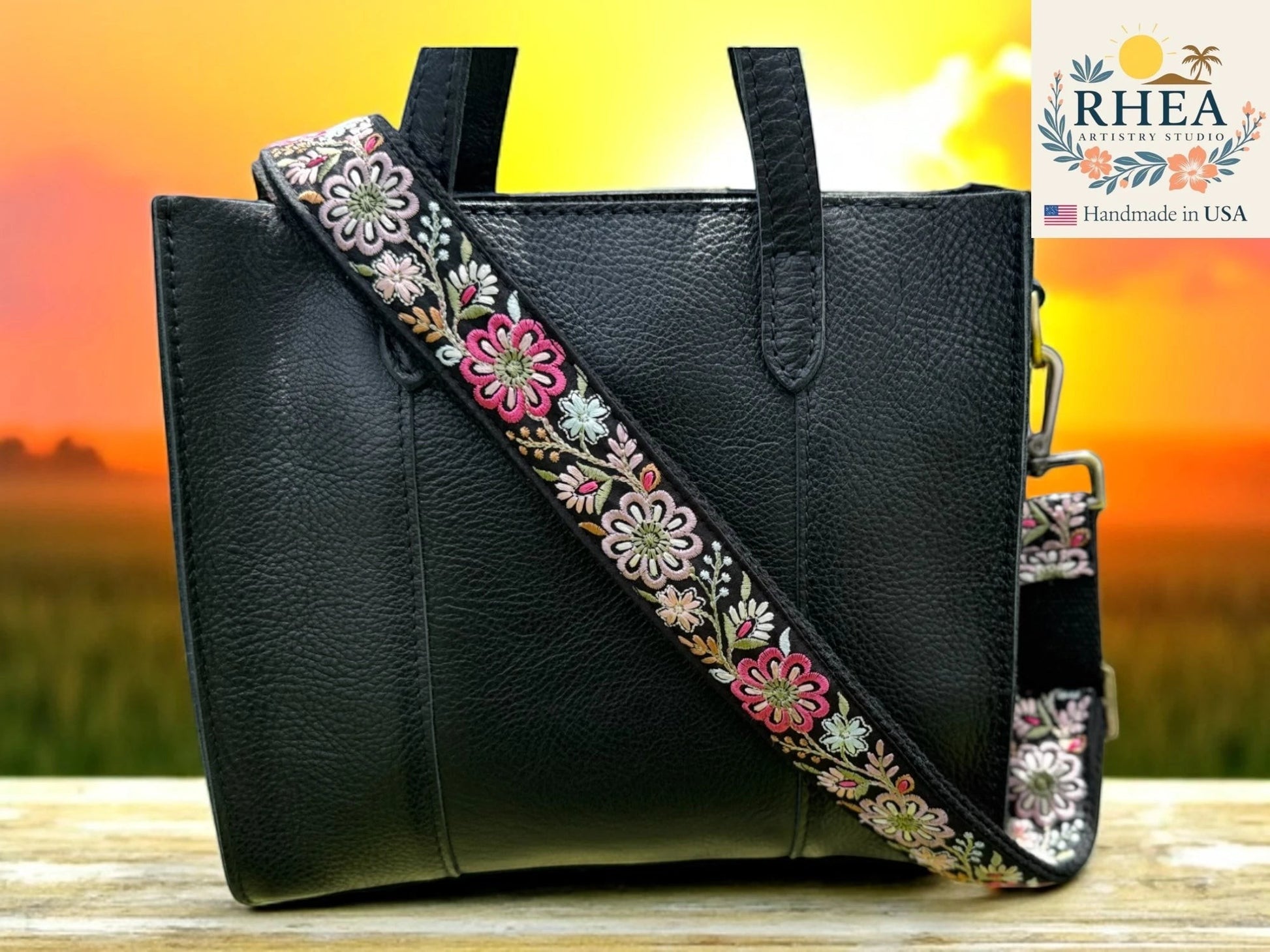 Rhea Artistry Studio 1.5-inch crossbody strap with embroidered pinwheel flowers in pink, white, and green on black webbing. Adjustable length with brass hooks.