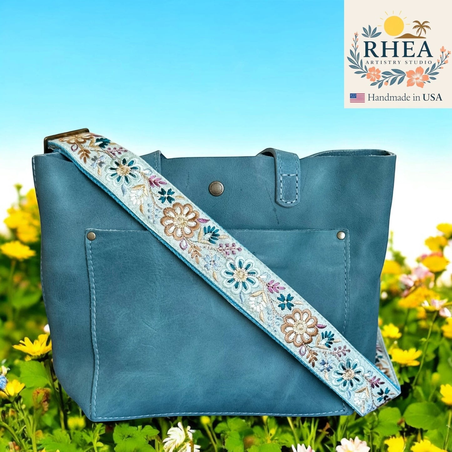 Rhea Artistry Studio light blue crossbody strap with embroidered pinwheel flowers in tan, white, and purple, 1.5-inch wide, adjustable 30-54 inches.