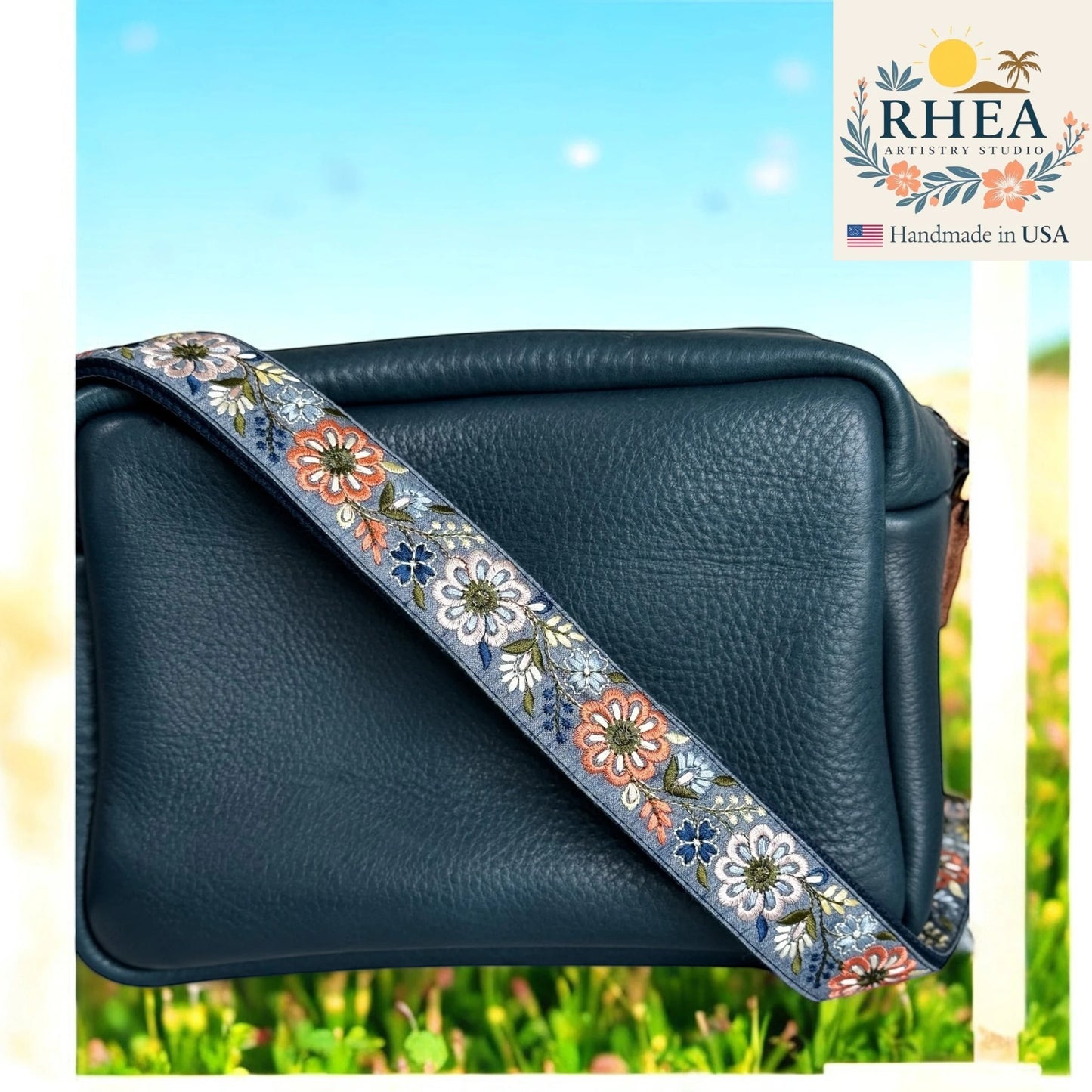 Rhea Artistry Studio 1.5-inch crossbody strap with embroidered pinwheel flowers in blue, orange, and white on a grey background.
