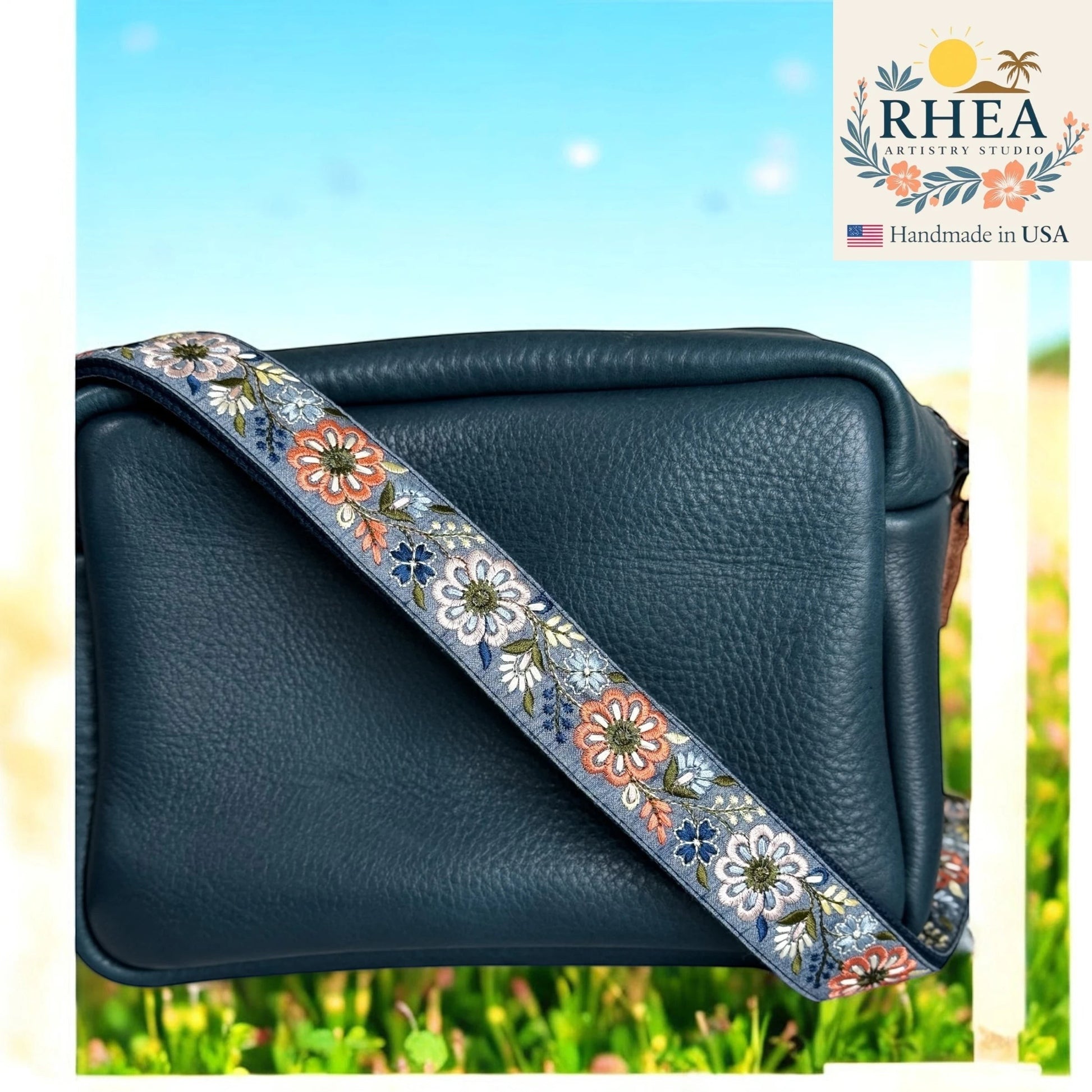 Rhea Artistry Studio 1.5-inch crossbody strap with embroidered pinwheel flowers in blue, orange, and white on a grey background.