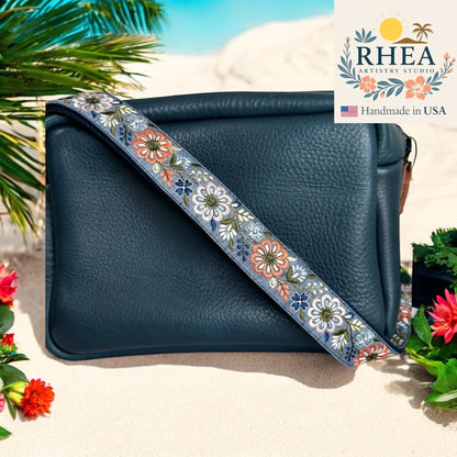Rhea Artistry Studio 1.5-inch crossbody strap with embroidered pinwheel flowers in blue, white, and coral on a denim-like background.