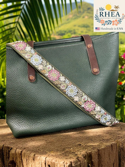 Rhea Artistry Studio 1.5-inch crossbody strap with embroidered pinwheel flowers in pink, blue, and white on a green background, with brushed brass hardware.