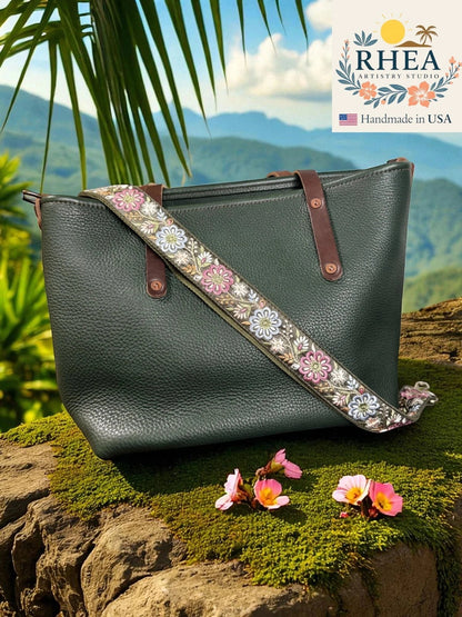 Rhea Artistry Studio 1.5-inch crossbody strap with embroidered pinwheel flowers in pink, white, and blue on a green background, featuring brushed brass hardware.