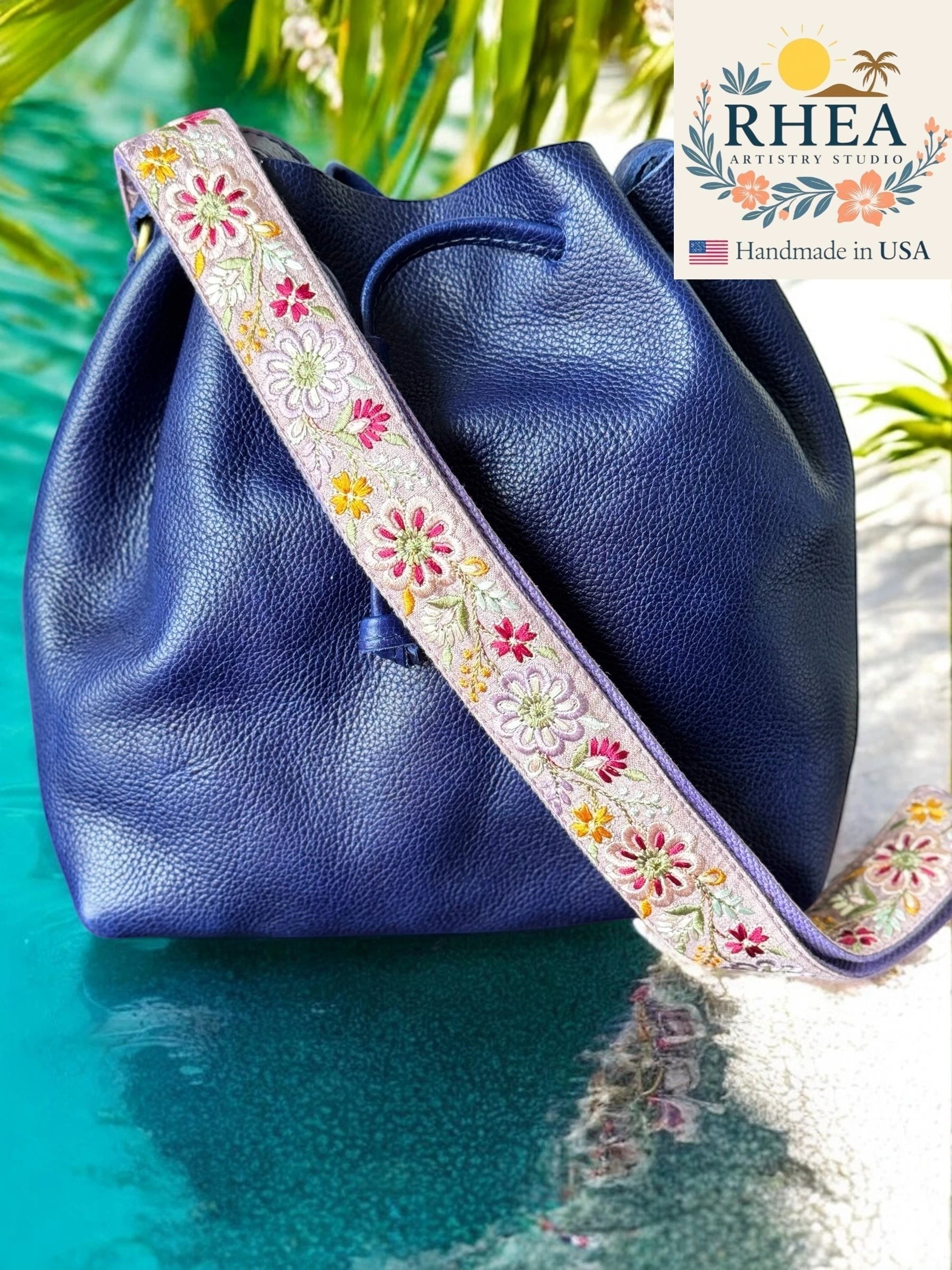 Rhea Artistry Studio 1.5-inch crossbody strap with embroidered pinwheel flowers in pink, yellow, and white on a light purple background.