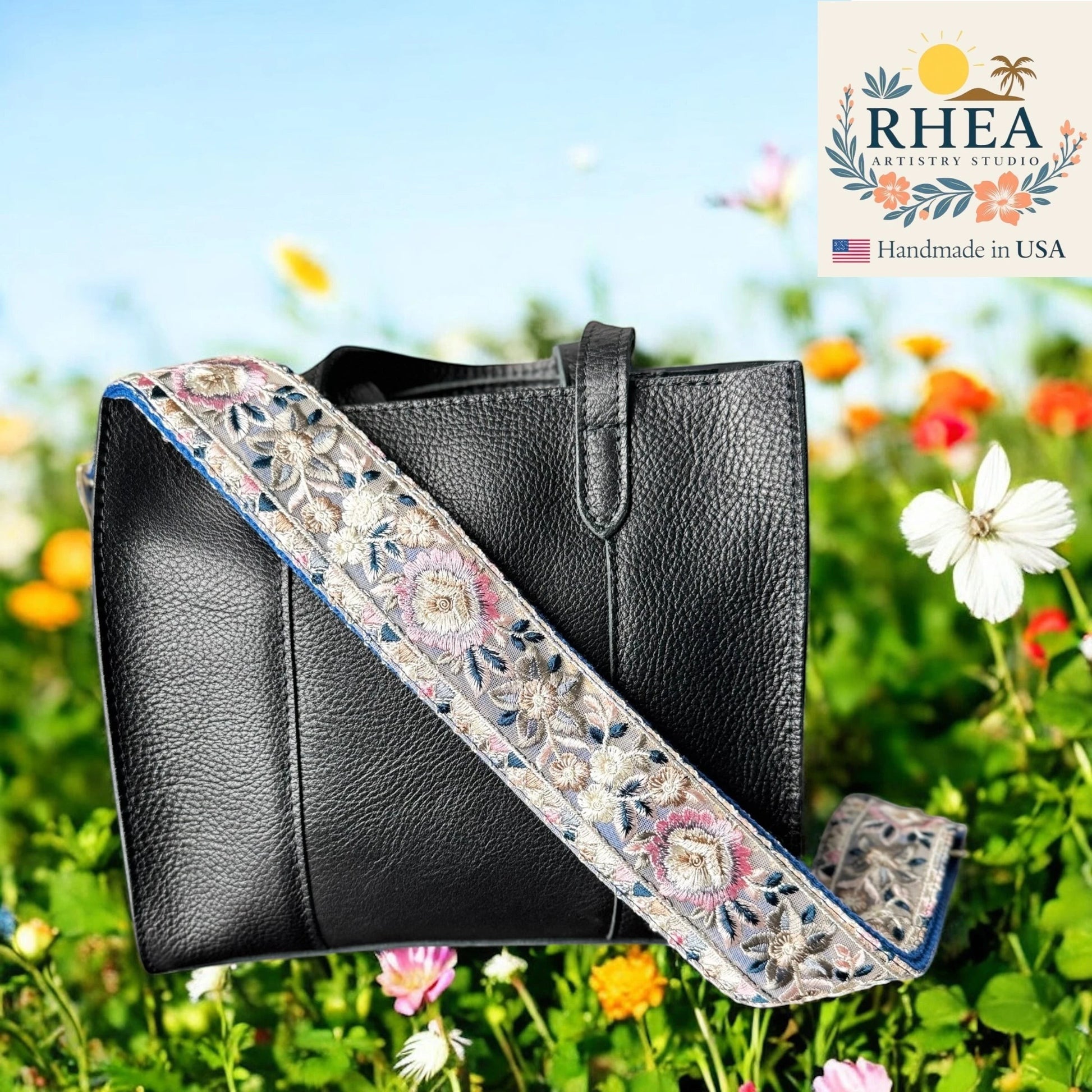 Rhea Artistry Studio 2-inch wide crossbody strap with intricate star flower embroidery in pink, blue, and white on a grey background. Adjustable length with brushed brass hardware.