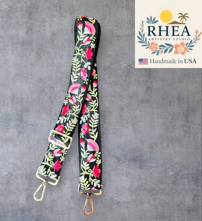 Rhea Artistry Studio black crossbody strap with embroidered pink roses and green leaves, 1.5-inch width, adjustable length, brushed brass hardware.