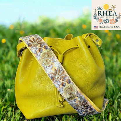 Rhea Artistry Studio 2-inch crossbody strap with rose bloom embroidery in gold, brown, and grey on a light yellow background. Adjustable purse strap.